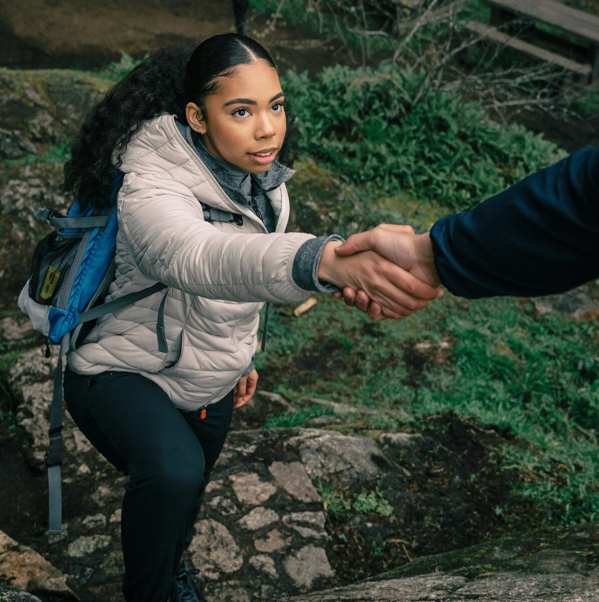 Young girl reaching up for help while climbing a mountain